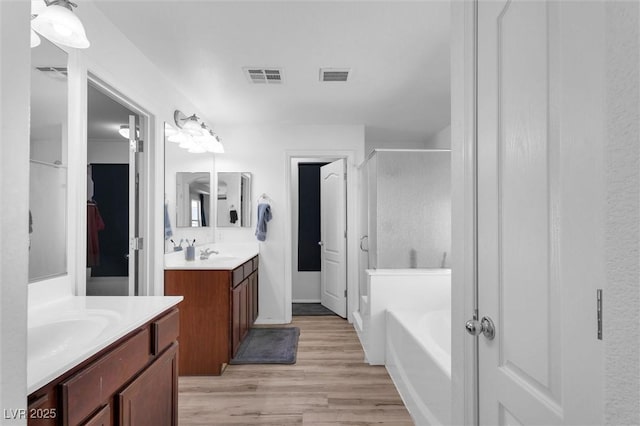 bathroom with a stall shower, wood finished floors, two vanities, and a garden tub
