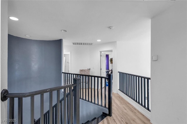 hall with an upstairs landing, wood finished floors, and recessed lighting