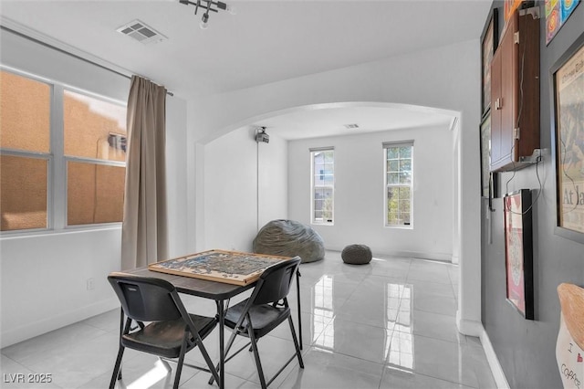 dining area featuring arched walkways, light tile patterned floors, and baseboards