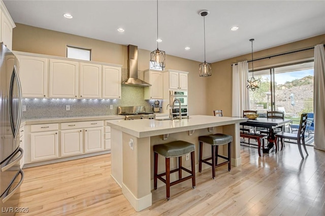 kitchen with wall chimney exhaust hood, light wood-style flooring, appliances with stainless steel finishes, decorative backsplash, and recessed lighting