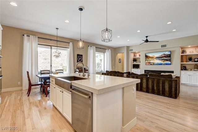 kitchen with stainless steel dishwasher, a sink, light countertops, a ceiling fan, and light wood-style flooring
