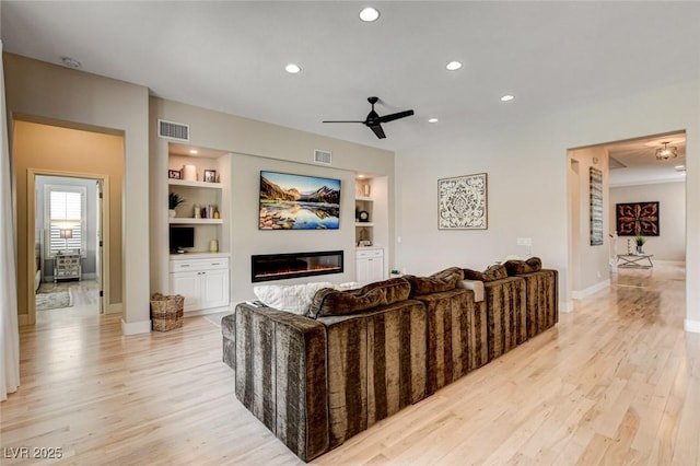 living room featuring ceiling fan, a glass covered fireplace, light wood-type flooring, recessed lighting, and baseboards