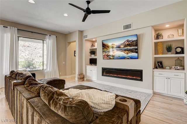 living room with a glass covered fireplace, built in features, light wood-style flooring, a ceiling fan, and recessed lighting