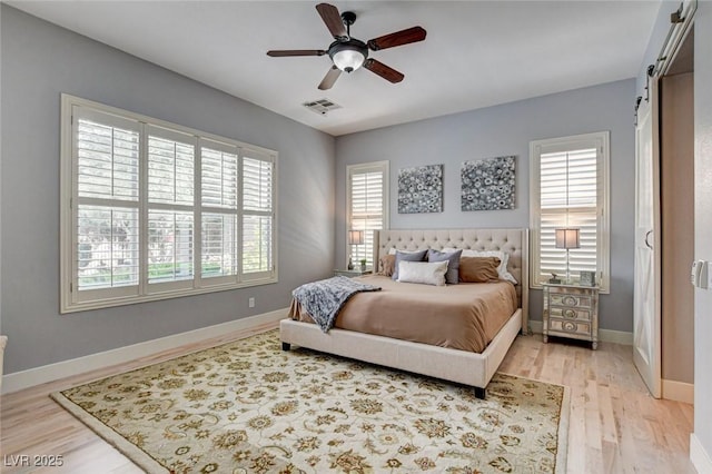 bedroom featuring a barn door, light wood-style flooring, baseboards, and a ceiling fan