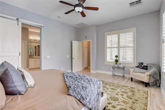 bedroom featuring light wood-type flooring, connected bathroom, a barn door, and a ceiling fan