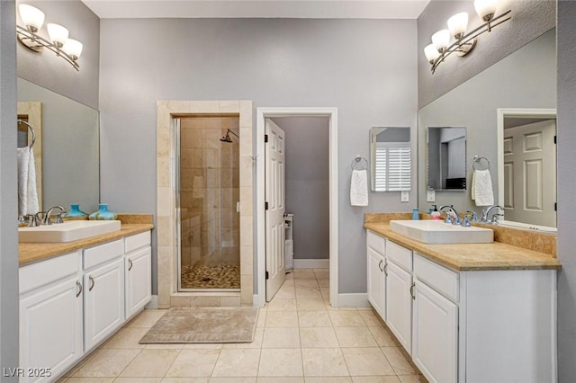 full bath with a stall shower, two vanities, tile patterned floors, and baseboards