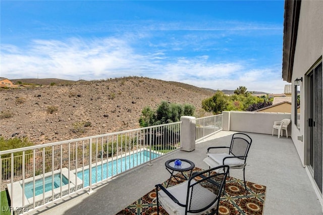 balcony featuring view of pool area, a pool with connected hot tub, a mountain view, and a patio area