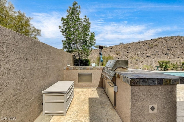 view of patio / terrace featuring fence, an outdoor kitchen, a mountain view, and a pool