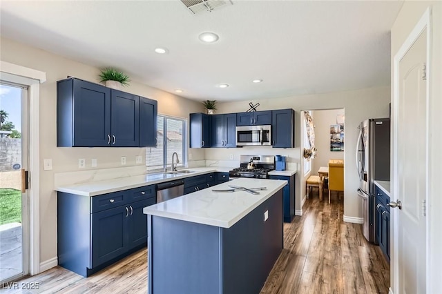 5502 Cinnamon Ave, Las Vegas, NV 89122 - kitchen with appliances with stainless steel finishes, blue cabinetry, a kitchen island, a sink, and light wood-style flooring
