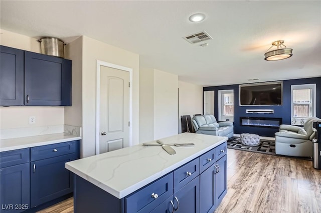 5502 Cinnamon Ave, Las Vegas, NV 89122 - kitchen with blue cabinetry, open floor plan, light wood-style floors, a center island, and light stone countertops