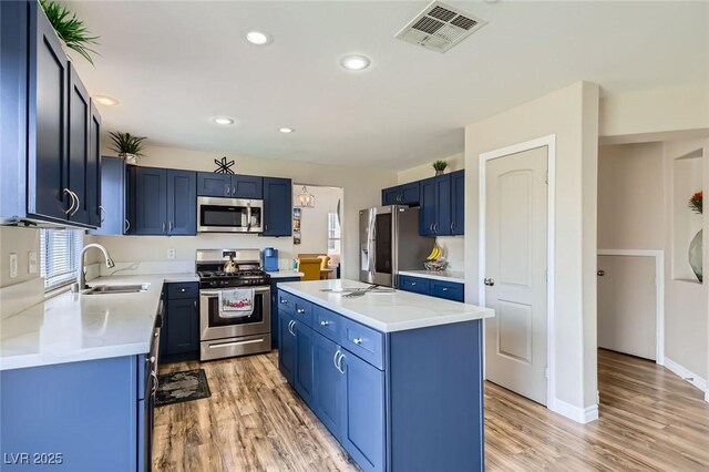 5502 Cinnamon Ave, Las Vegas, NV 89122 - kitchen with stainless steel appliances, a sink, blue cabinetry, light wood-type flooring, and a kitchen island