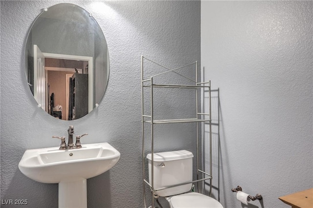 bathroom featuring a textured wall, a sink, and toilet