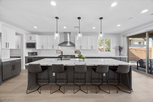 10470 Dove Meadow Way, Las Vegas, NV 89135 - kitchen with wall chimney range hood, stainless steel microwave, white cabinets, a sink, and a kitchen island with sink