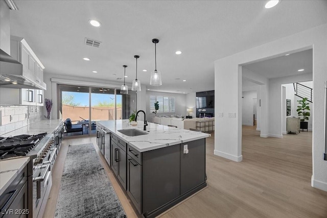 10470 Dove Meadow Way, Las Vegas, NV 89135 - kitchen with a sink, wall chimney range hood, range with two ovens, a kitchen island with sink, and light wood-style flooring
