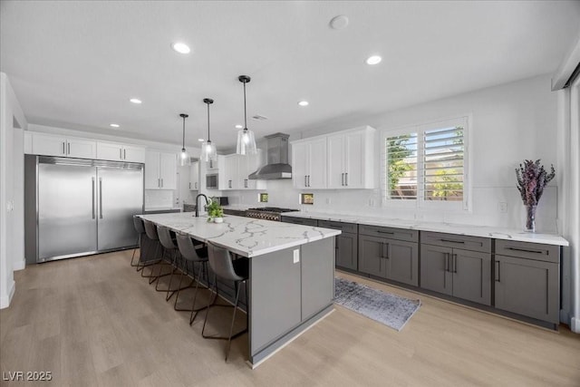 10470 Dove Meadow Way, Las Vegas, NV 89135 - kitchen with appliances with stainless steel finishes, wall chimney range hood, light wood finished floors, white cabinetry, and light stone counters