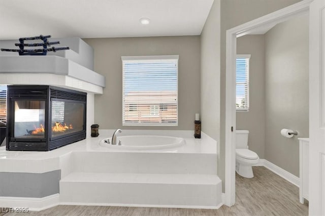 7310 Heggie Ave, Las Vegas, NV 89131 - full bath with a garden tub, toilet, a multi sided fireplace, wood finished floors, and healthy amount of natural light