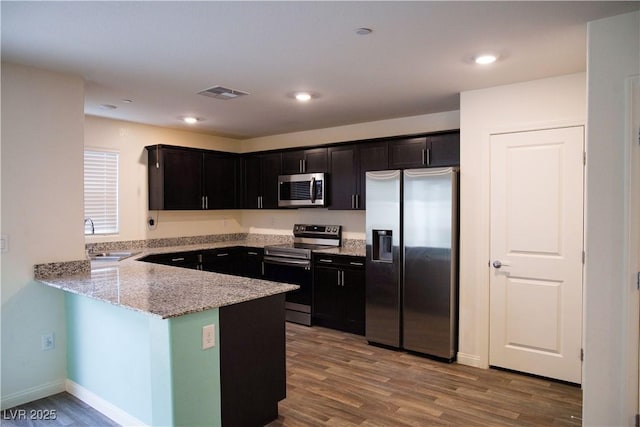 kitchen featuring appliances with stainless steel finishes, a sink, light stone counters, wood finished floors, and a peninsula