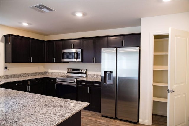kitchen with appliances with stainless steel finishes, light wood-style floors, light stone counters, and recessed lighting