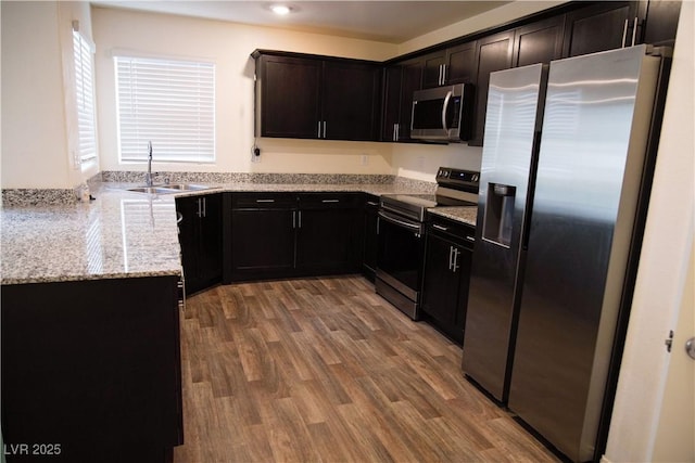 kitchen featuring appliances with stainless steel finishes, a sink, light stone counters, and wood finished floors