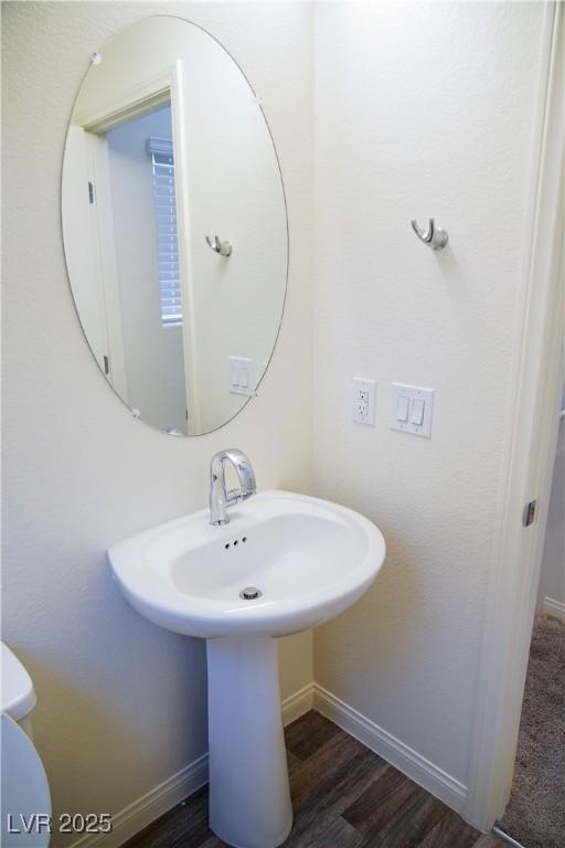 half bathroom with baseboards, wood finished floors, a sink, and toilet