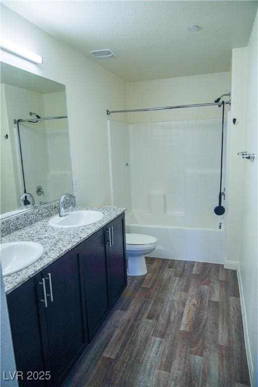 bathroom featuring wood finished floors, double vanity, toilet, and  shower combination