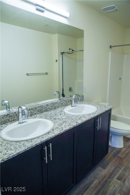 full bath with wood finished floors, double vanity, toilet, and shower / bathtub combination
