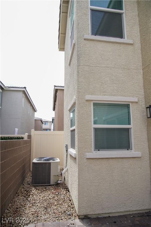 view of side of home with stucco siding, central AC unit, and fence