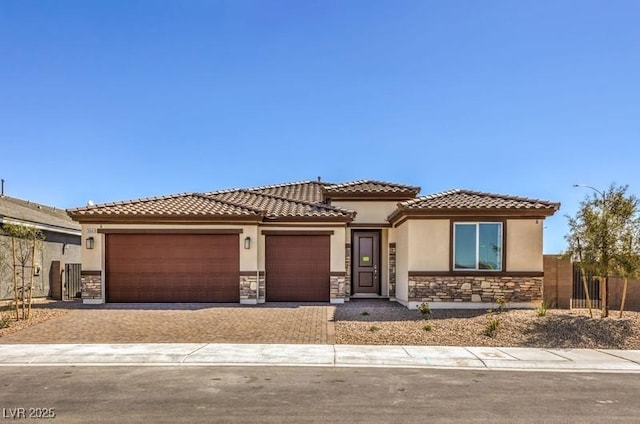 1220 Eva Creek Dr Unit 35, North Las Vegas, NV 89084 - view of front of home with stone siding, an attached garage, stucco siding, driveway, and fence