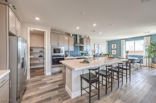 1220 Eva Creek Dr Unit 35, North Las Vegas, NV 89084 - kitchen featuring appliances with stainless steel finishes, wall chimney exhaust hood, light wood finished floors, a breakfast bar area, and gray cabinets