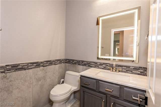 half bath with tile walls, toilet, a wainscoted wall, and vanity