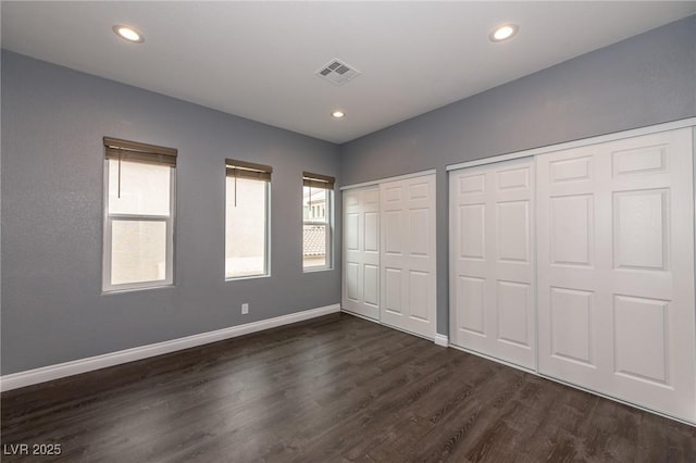 unfurnished bedroom with multiple closets, dark wood-style floors, baseboards, and recessed lighting