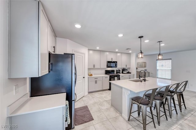 kitchen featuring black appliances, a sink, a kitchen breakfast bar, light countertops, and a kitchen island with sink
