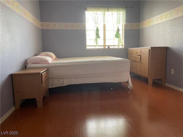 bedroom featuring wood finished floors, a textured wall, and baseboards