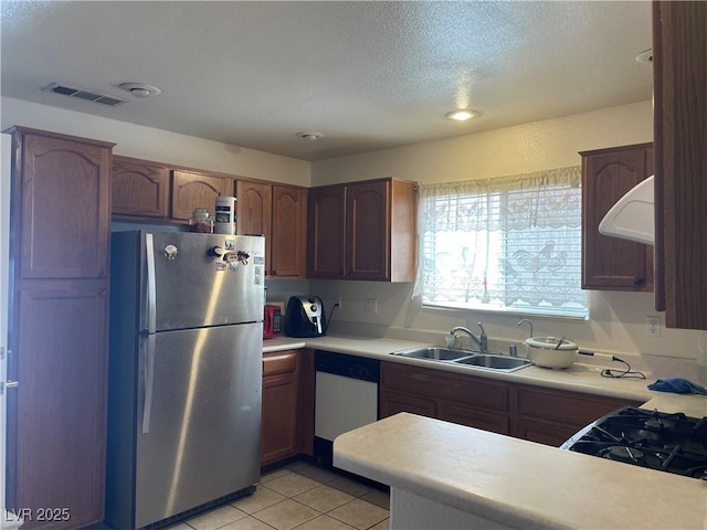 kitchen with freestanding refrigerator, a sink, dishwashing machine, exhaust hood, and light countertops