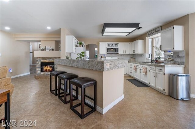 4209 Glass Lantern Dr, North Las Vegas, NV 89032 - kitchen with stainless steel microwave, a sink, a breakfast bar area, open shelves, and a stone fireplace
