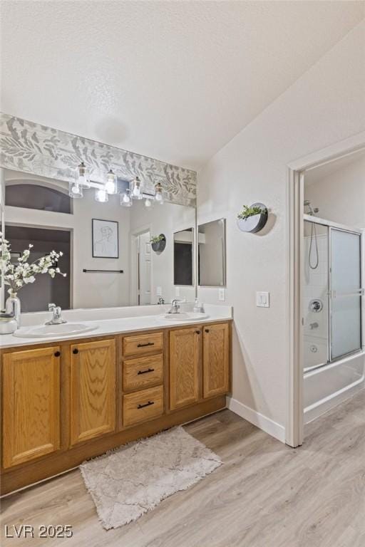 bathroom with wood finished floors, double vanity, shower / bath combination with glass door, and baseboards