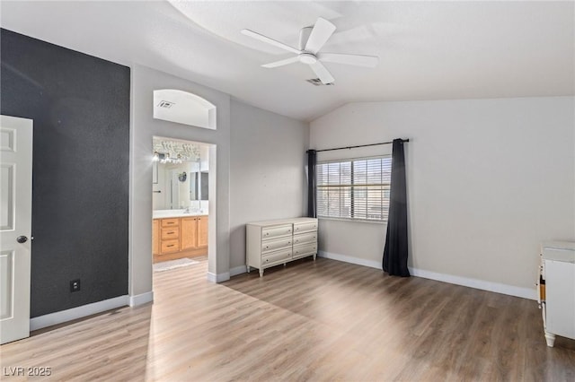 unfurnished bedroom with lofted ceiling, light wood finished floors, baseboards, ensuite bath, and ceiling fan