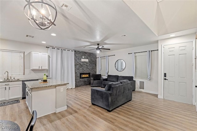 living area with a ceiling fan, a chandelier, light wood-type flooring, a stone fireplace, and recessed lighting