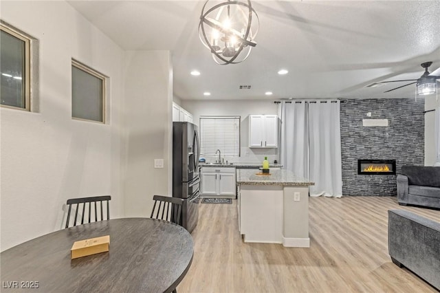 kitchen with open floor plan, a center island, ceiling fan, light wood-type flooring, and a large fireplace