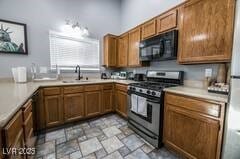 1012 Greystone Dr, Las Vegas, NV 89108 - kitchen with black microwave, stainless steel range with gas stovetop, brown cabinets, light countertops, and a sink