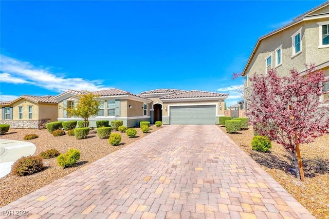 mediterranean / spanish home featuring stucco siding, decorative driveway, a tiled roof, an attached garage, and a residential view