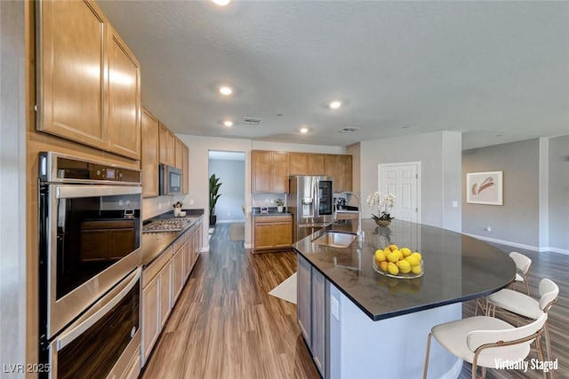 kitchen featuring appliances with stainless steel finishes, dark wood finished floors, a breakfast bar area, baseboards, and recessed lighting