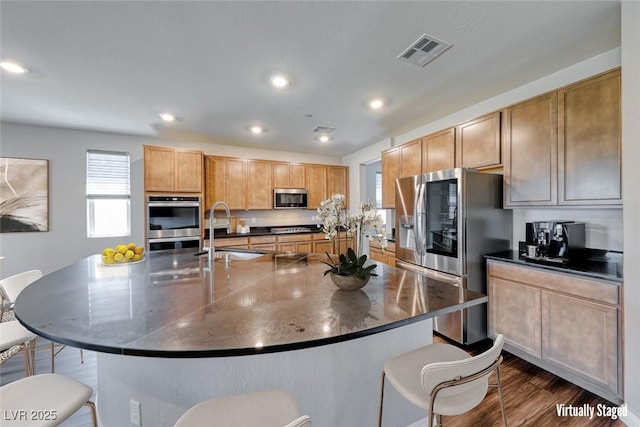 kitchen featuring appliances with stainless steel finishes, a sink, a breakfast bar, dark countertops, and a large island