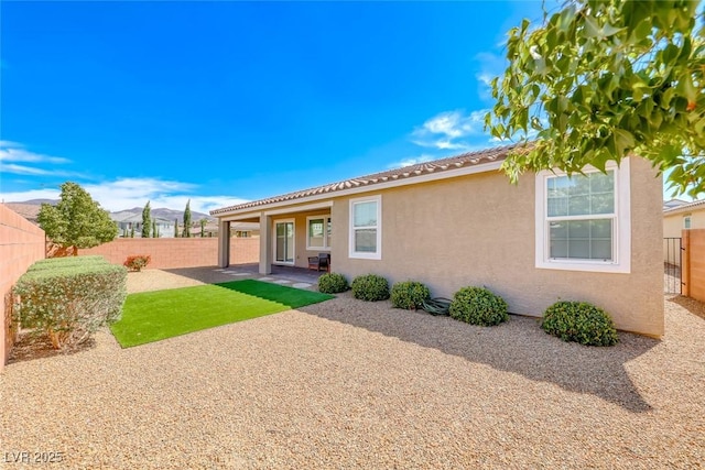 rear view of property featuring stucco siding, a fenced backyard, a patio area, and a tile roof