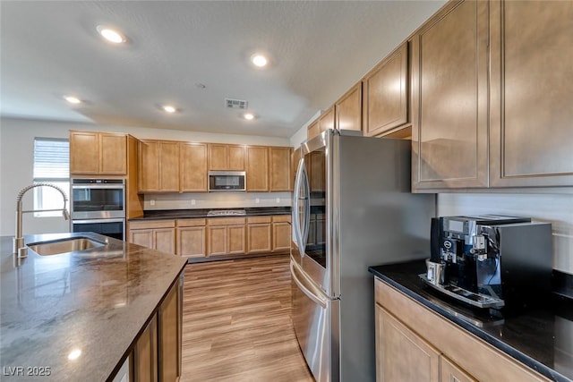 kitchen featuring stainless steel appliances, light wood-type flooring, dark stone counters, a sink, and recessed lighting