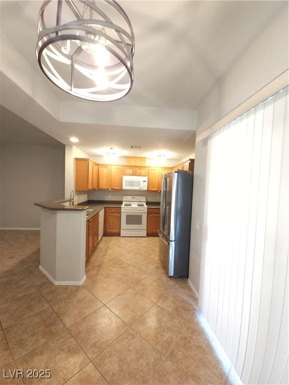 4675 Basilicata Ln Unit 103, North Las Vegas, NV 89084 - kitchen featuring white appliances, dark countertops, a peninsula, light tile patterned floors, and baseboards