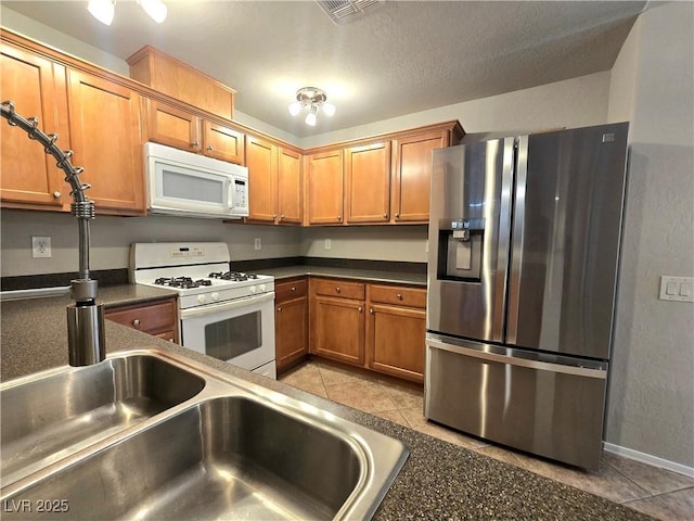 4675 Basilicata Ln Unit 103, North Las Vegas, NV 89084 - kitchen with white appliances, light tile patterned floors, dark countertops, brown cabinets, and baseboards