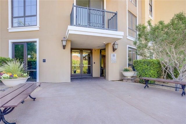 property entrance with french doors, stucco siding, a balcony, and a patio area