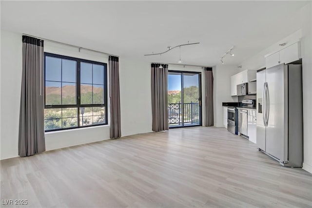 unfurnished living room with rail lighting and light wood-style flooring