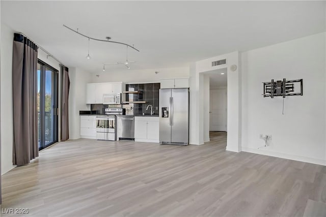 kitchen with stainless steel appliances, dark countertops, a sink, open shelves, and white cabinetry